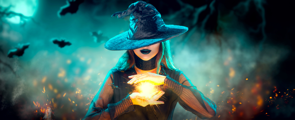 Halloween Witch girl with making witchcraft, magic in her hands, spells. Beautiful young woman in witches hat conjuring. Spooky dark magic forest background. Magician. Wide Halloween party art design